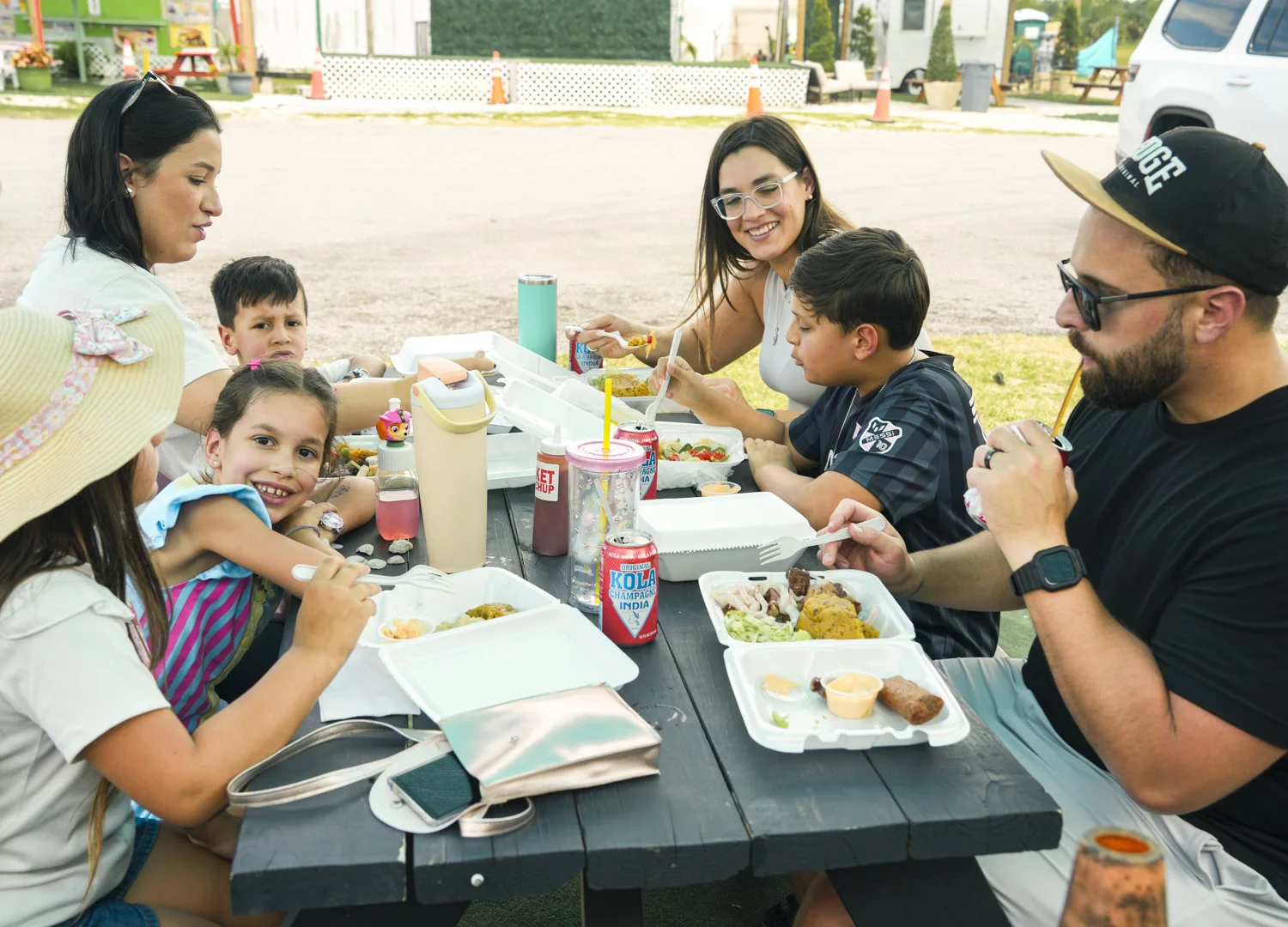A family sits around an outdoor table, laughing and enjoying a meal together. The scene conveys a feeling of joy, togetherness, and happy moments shared.
