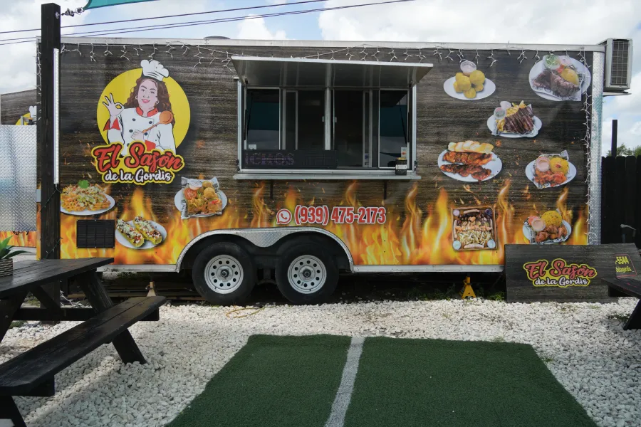 A food truck with an open service window, ready to serve customers. Details of its design and the menu available for sale can be seen.