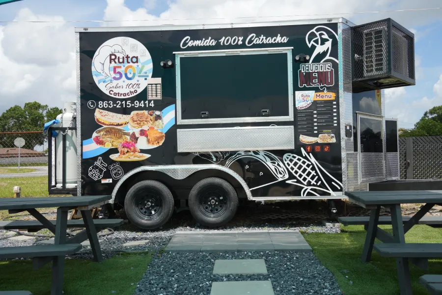 A food truck is parked, standing out for its modern and discreet design. Despite its dark color, details of its equipment for selling food on the street can be seen.