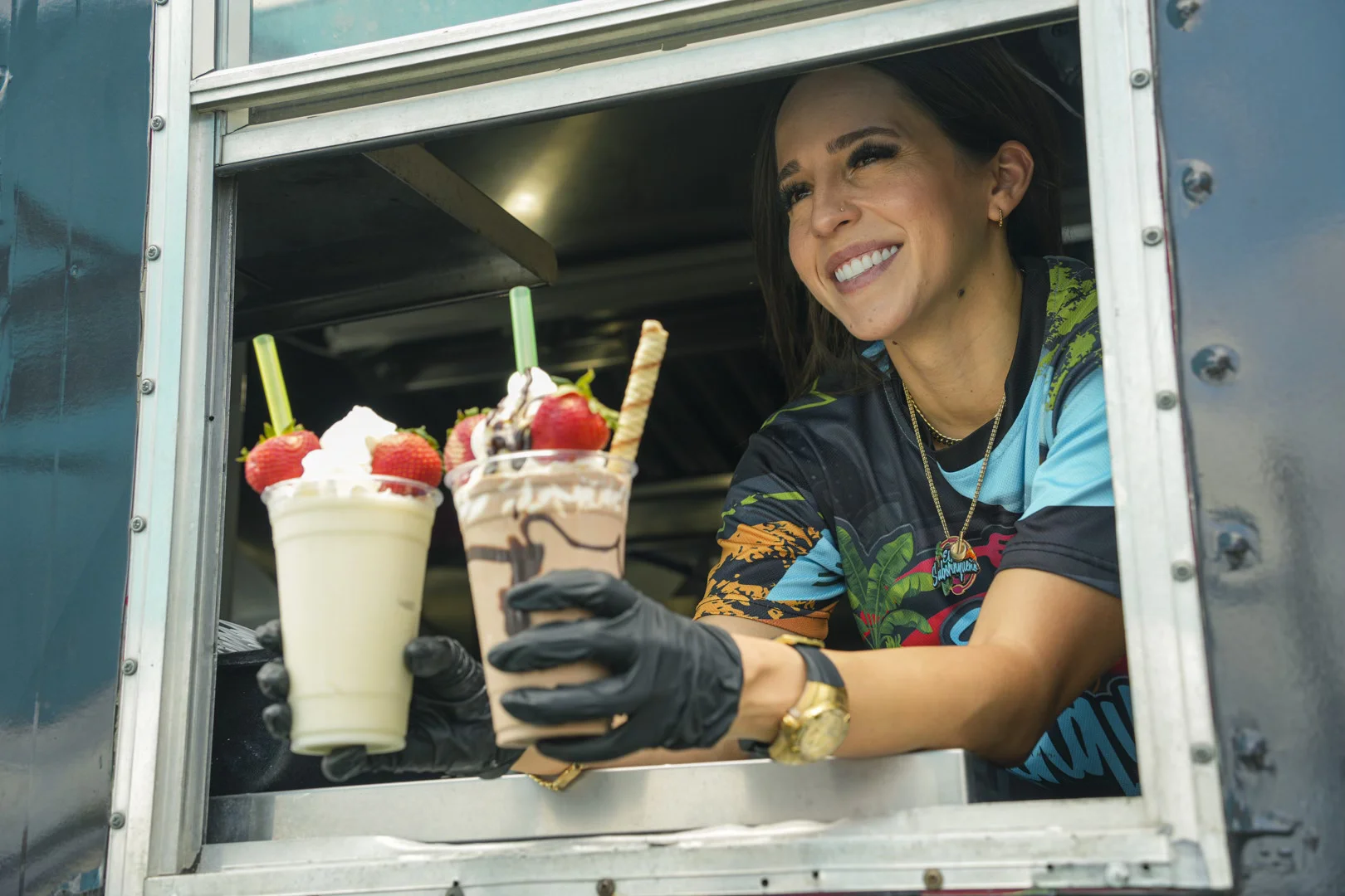 A friendly, smiling woman serves and hands two freshly made ice creams to a customer, displaying a cordial transaction and a refreshing, delicious product.